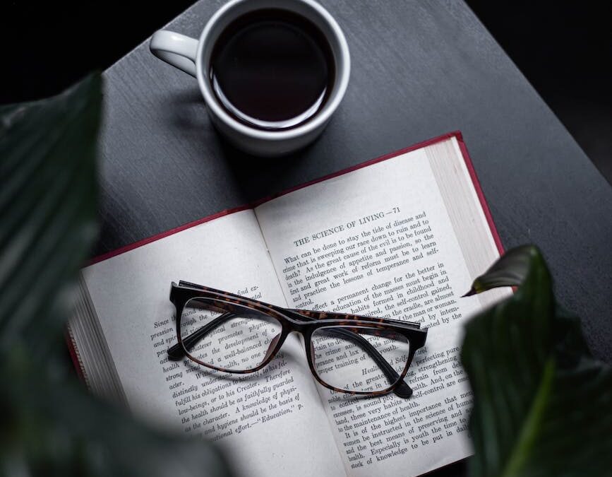 eyeglasses on opened book beside cup of coffee on table